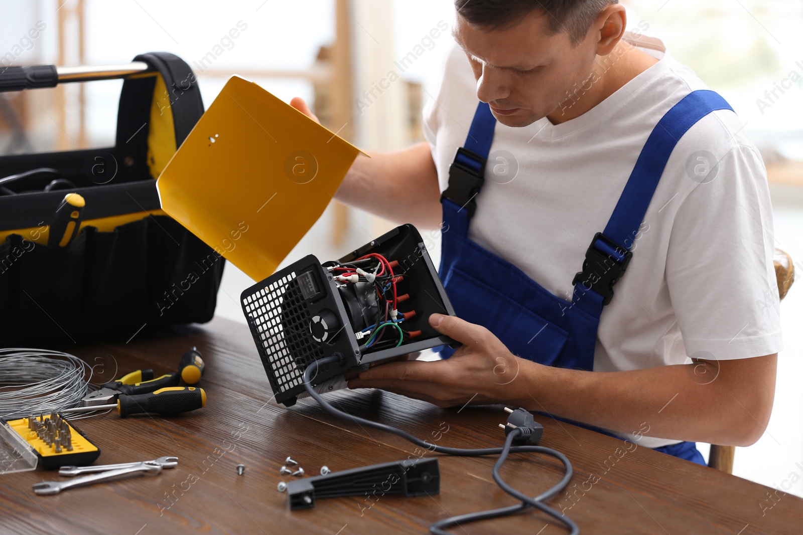 Photo of Professional technician repairing electric fan heater at table indoors