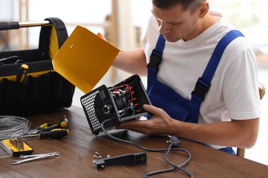 Professional technician repairing electric fan heater at table indoors