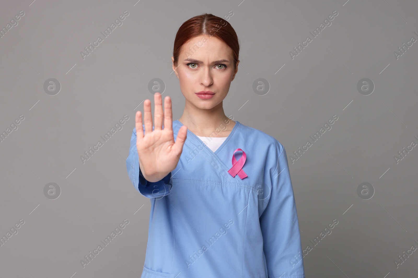Photo of Mammologist with pink ribbon showing stop gesture on gray background. Breast cancer awareness