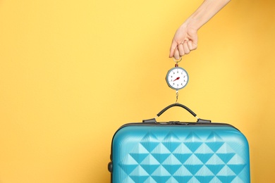 Woman weighing suitcase against color background, closeup. Space for text