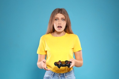 Emotional young woman playing video games with controller on color background