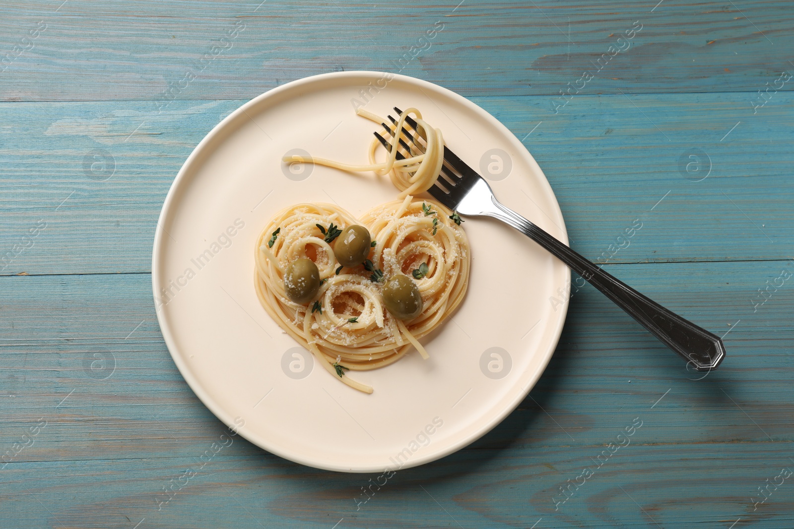 Photo of Heart made of tasty spaghetti, fork, olives and cheese on light blue wooden table, top view