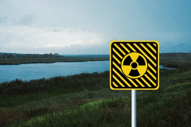 Radioactive pollution. Yellow warning sign with hazard symbol near river outdoors