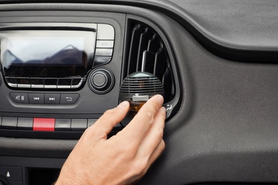 Photo of Man regulating air freshener near ventilation in car, closeup