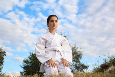 Cute little girl in kimono meditating outdoors. Karate practicing