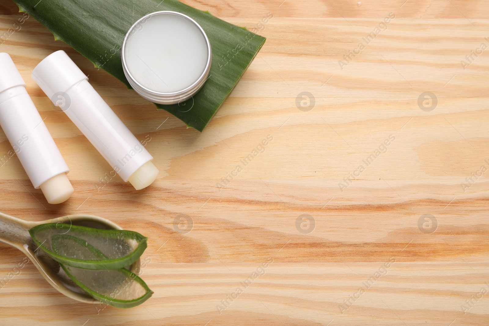 Photo of Different lip balms and aloe vera plant on wooden background, flat lay. Space for text