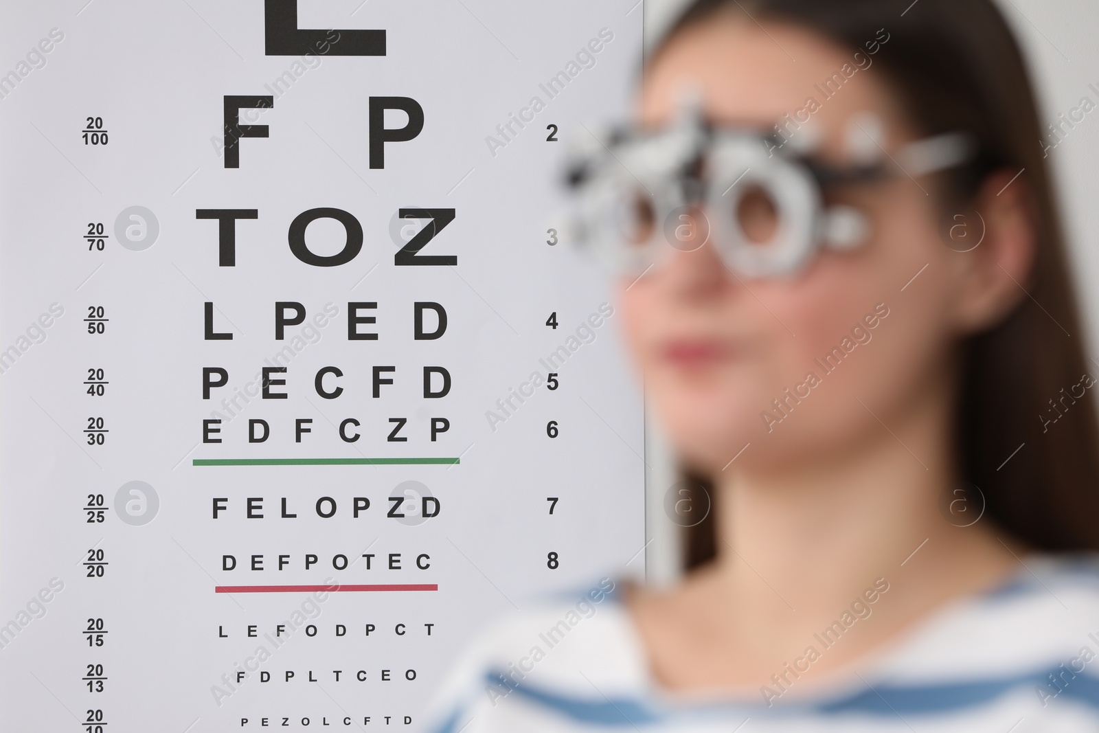 Photo of Young woman with trial frame against vision test chart, selective focus