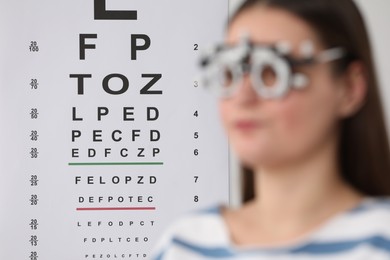 Photo of Young woman with trial frame against vision test chart, selective focus