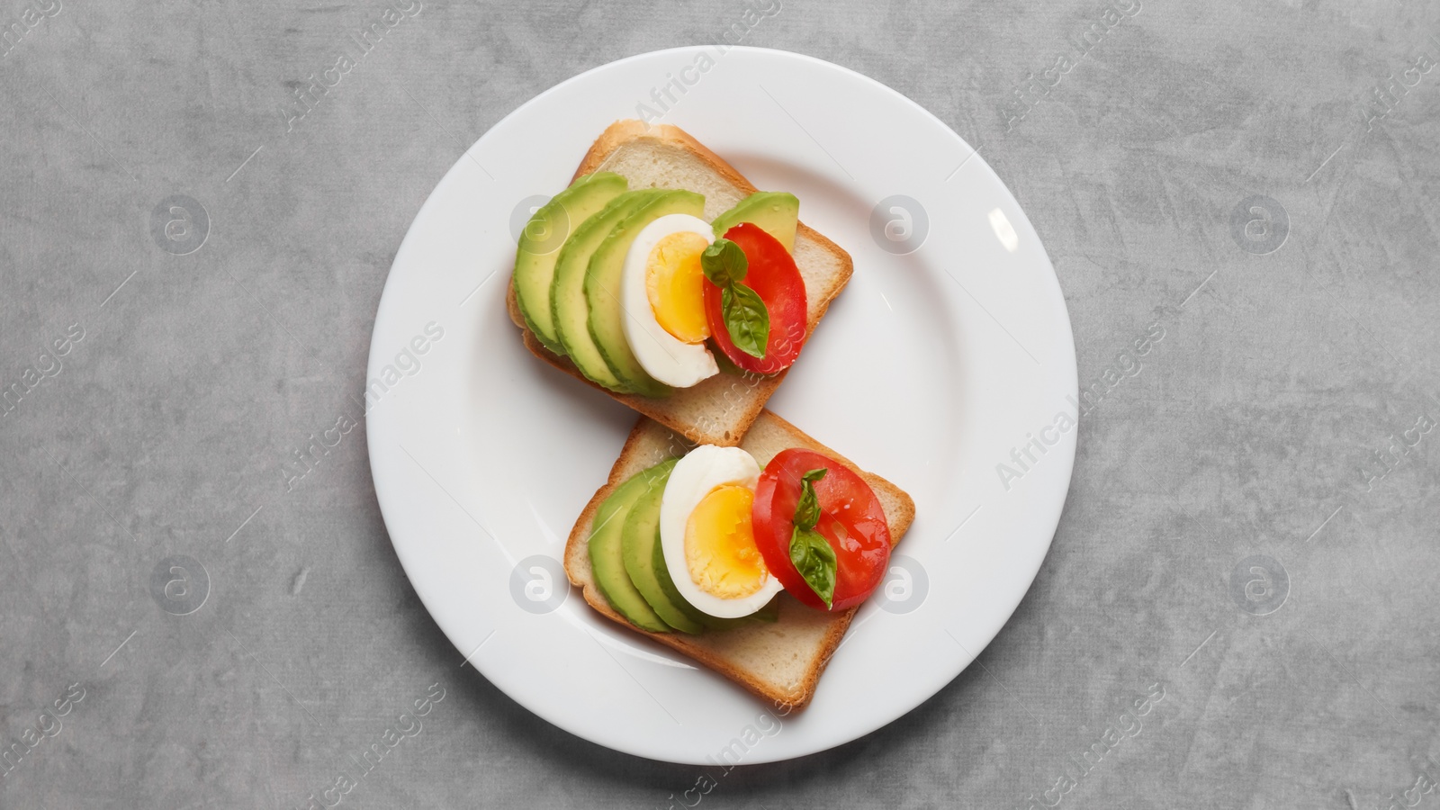 Photo of Tasty sandwiches with boiled egg, avocado and tomato on grey table, top view