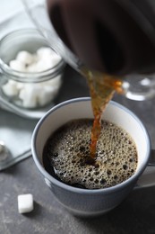 Photo of Pouring hot coffee into cup on grey table, closeup