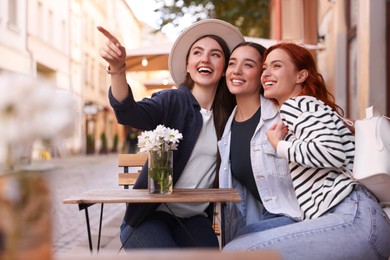 Photo of Smiling woman pointing at something to her friends in outdoor cafe
