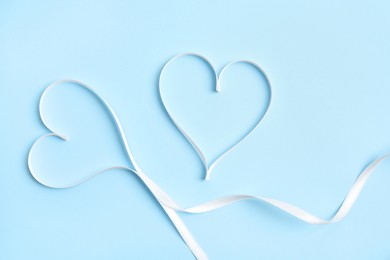 Photo of Hearts made of white ribbon on light blue background, flat lay. Valentine's day celebration