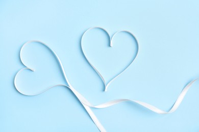 Hearts made of white ribbon on light blue background, flat lay. Valentine's day celebration