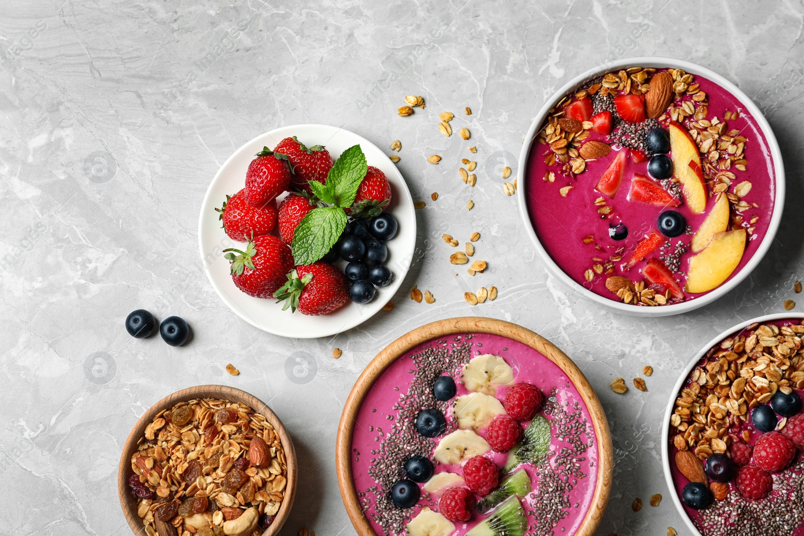 Photo of Acai smoothie bowls with granola and berries on marble table, flat lay