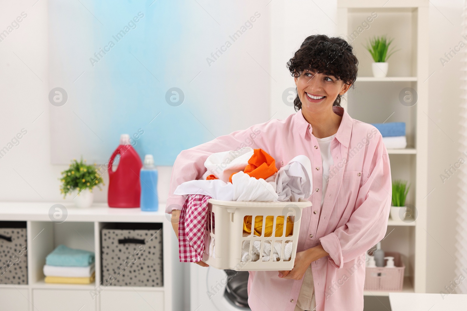 Photo of Happy woman with laundry basket full of clothes indoors, space for text