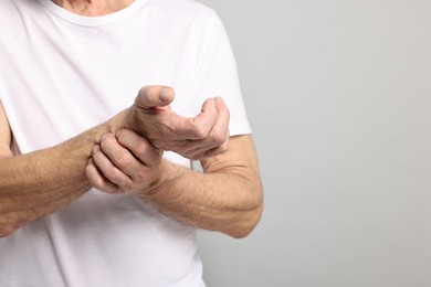 Photo of Arthritis symptoms. Man suffering from pain in wrist on gray background, closeup. Space for text