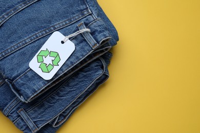Photo of Jeans with recycling label on yellow background, top view. Space for text
