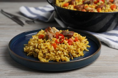 Delicious pilaf with meat, carrot and chili pepper on wooden table, closeup