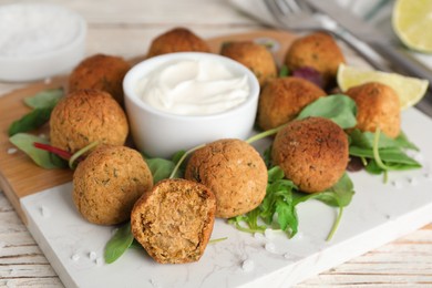 Photo of Delicious falafel balls with herbs, lime and sauce on wooden table, closeup