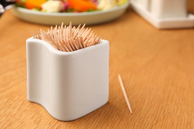 Holder with many toothpicks on wooden table, closeup. Space for text