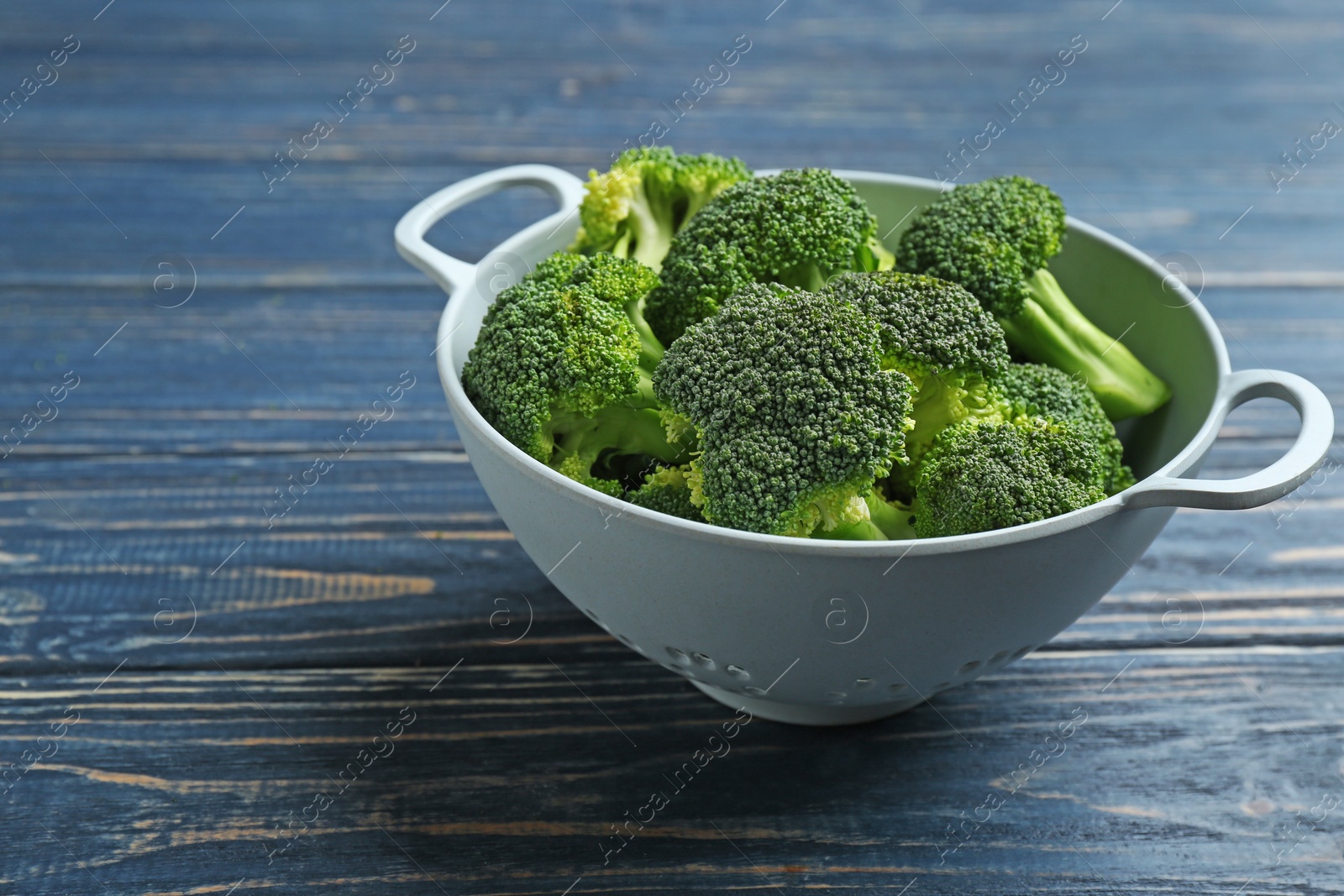 Photo of Colander of fresh broccoli on blue wooden table. Space for text