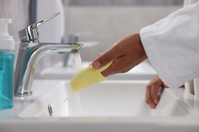 Photo of Young man cleaning face sponge above sink in bathroom, closeup