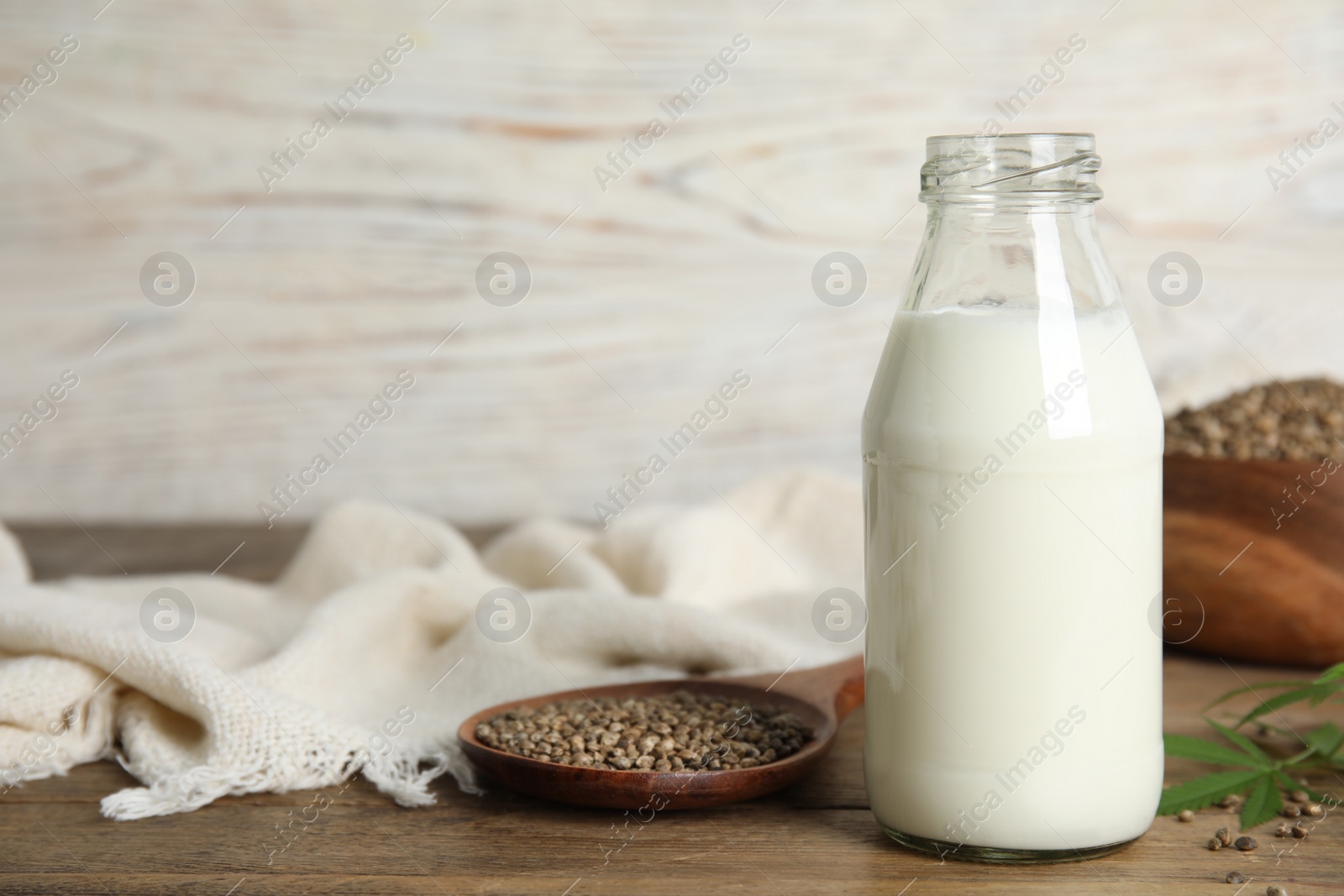 Photo of Glass bottle of hemp milk, seeds and leaves on wooden table. Space for text