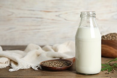 Glass bottle of hemp milk, seeds and leaves on wooden table. Space for text