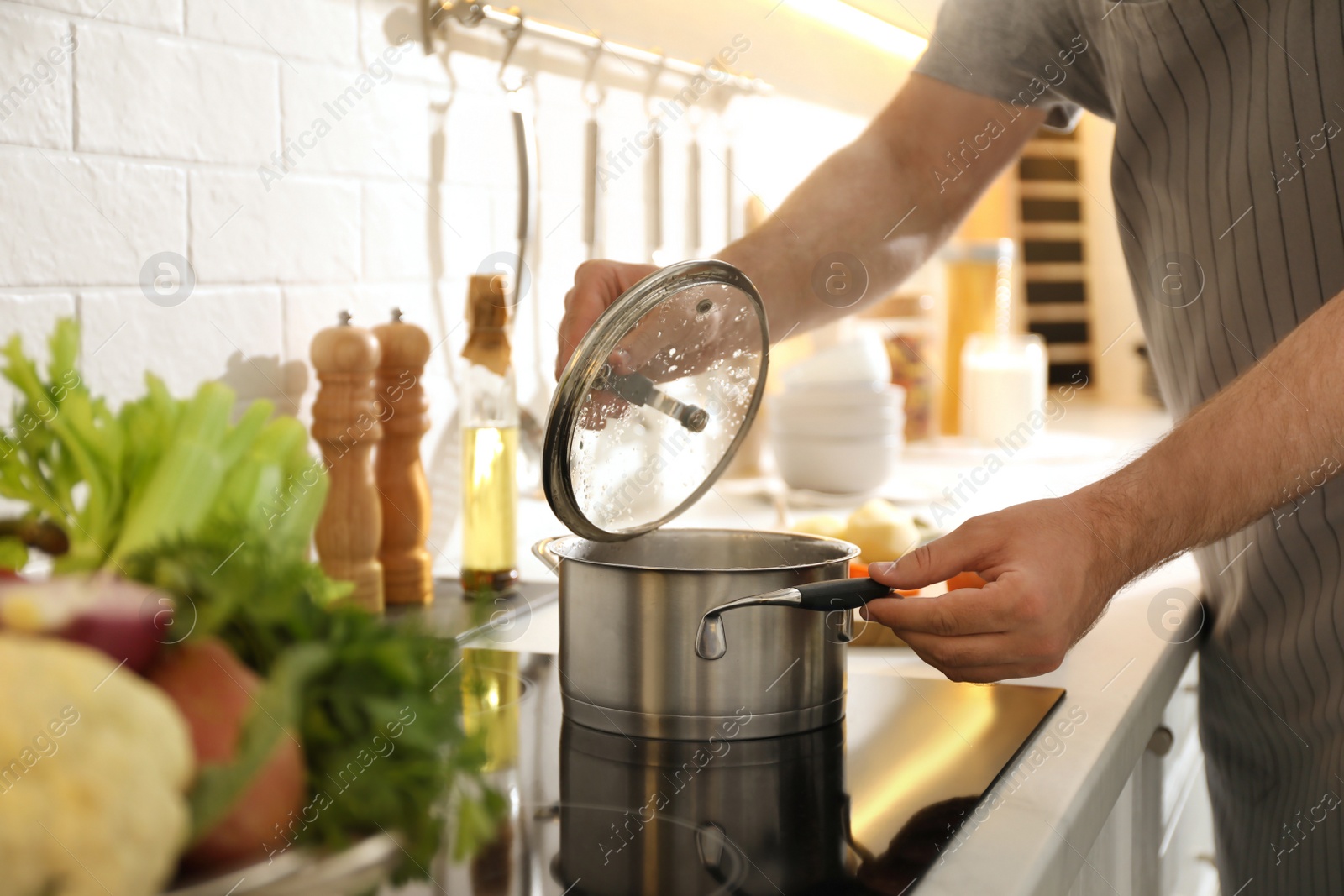 Photo of Man opening pot with fresh bouillon in kitchen, closeup. Homemade recipe