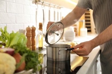 Man opening pot with fresh bouillon in kitchen, closeup. Homemade recipe