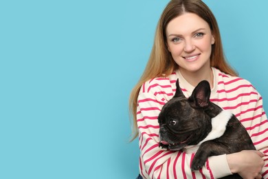 Portrait of happy woman hugging cute French Bulldog on light blue background, space for text