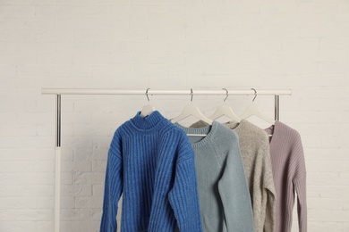 Collection of warm sweaters hanging on rack against white brick wall