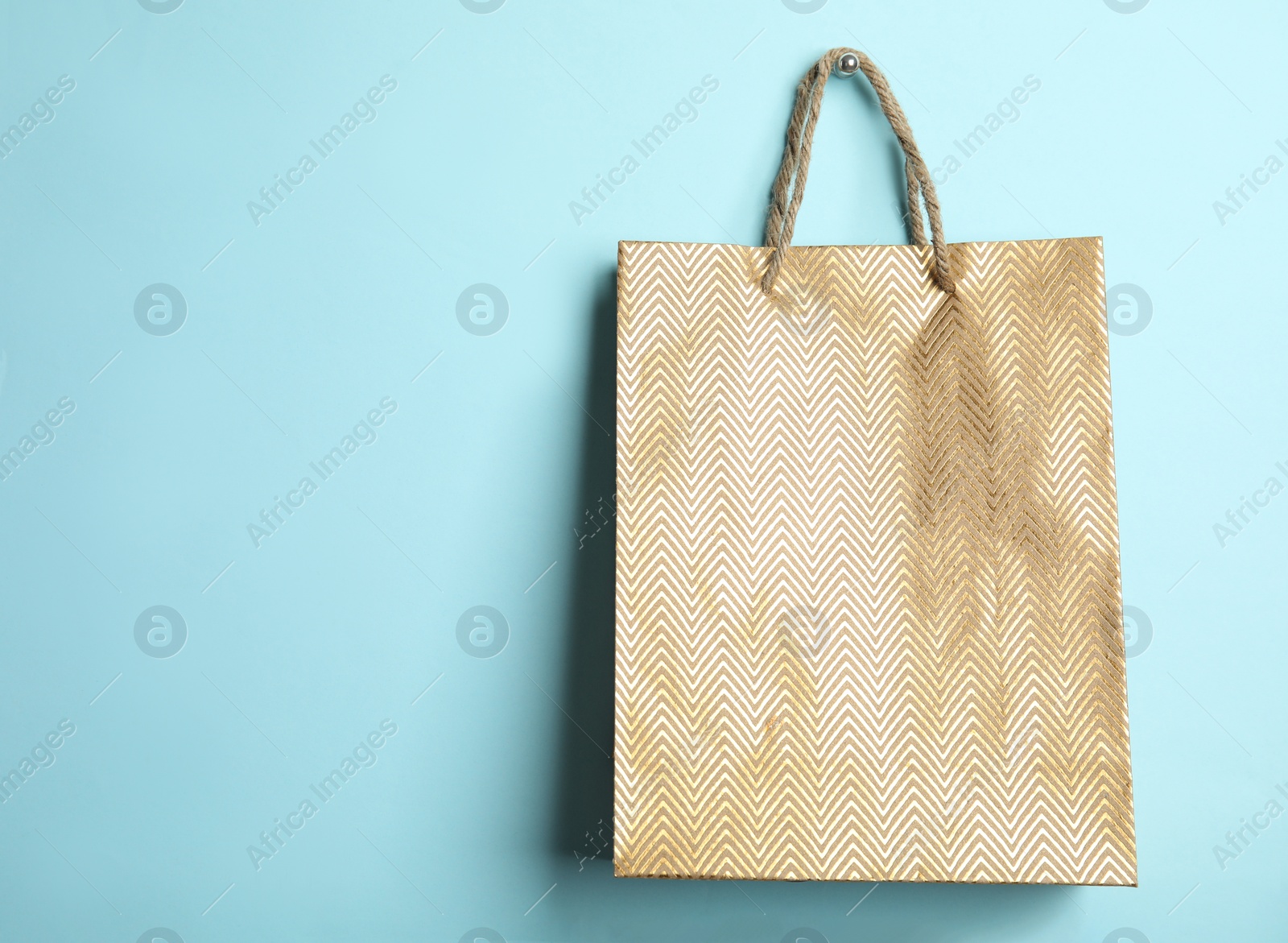 Photo of Gold shopping paper bag on light blue background, space for text