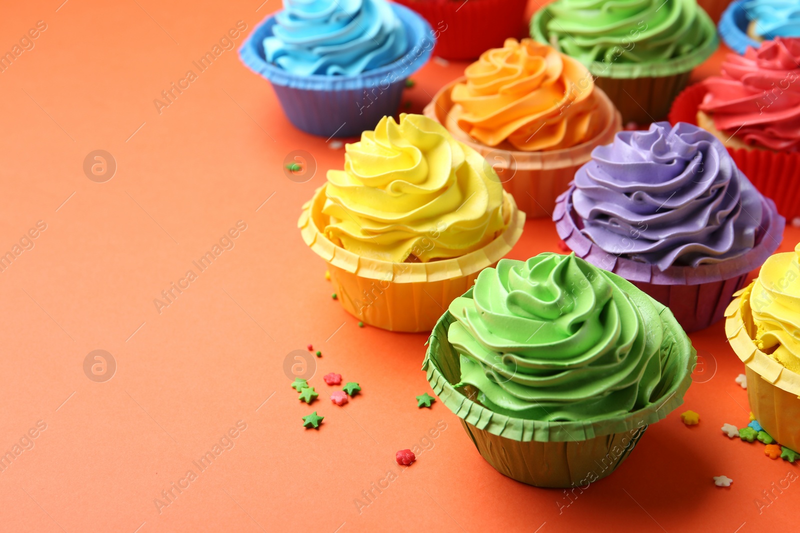 Photo of Delicious bright cupcakes and sprinkles on coral background, closeup. Space for text