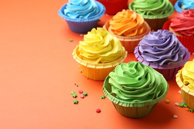 Photo of Delicious bright cupcakes and sprinkles on coral background, closeup. Space for text