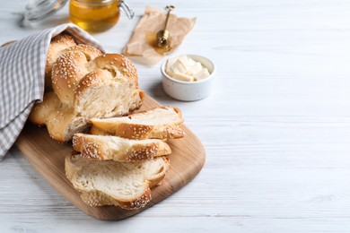 Photo of Cut freshly baked braided bread and butter on white wooden table, space for text. Traditional Shabbat challah