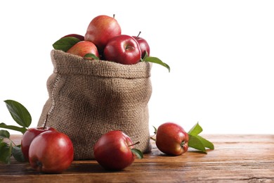 Photo of Ripe red apples with leaves in sack on wooden table against white background. Space for text