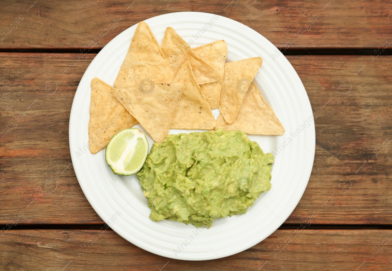 Photo of Delicious guacamole made of avocados, nachos and lime on wooden table, top view