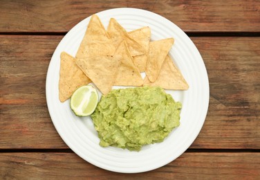 Delicious guacamole made of avocados, nachos and lime on wooden table, top view