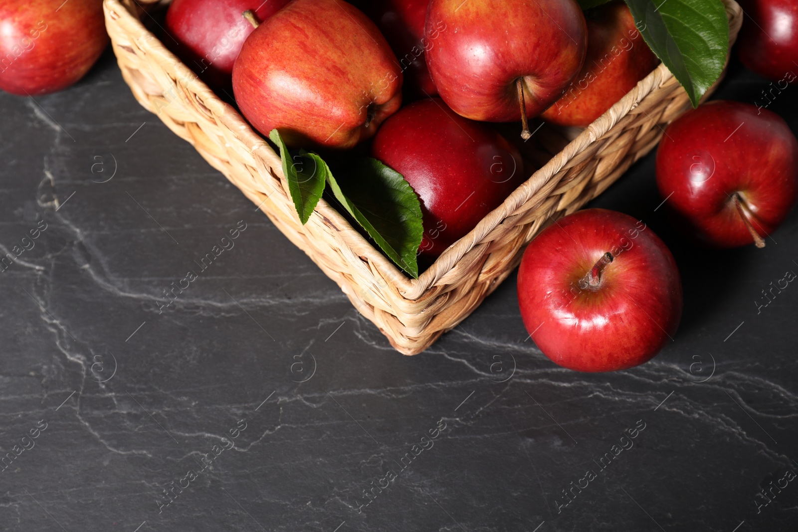 Photo of Fresh red apples in basket on dark grey table. Space for text