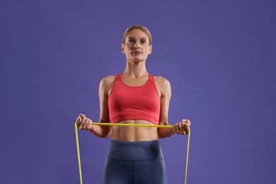Athletic woman exercising with elastic resistance band on purple background, low angle view