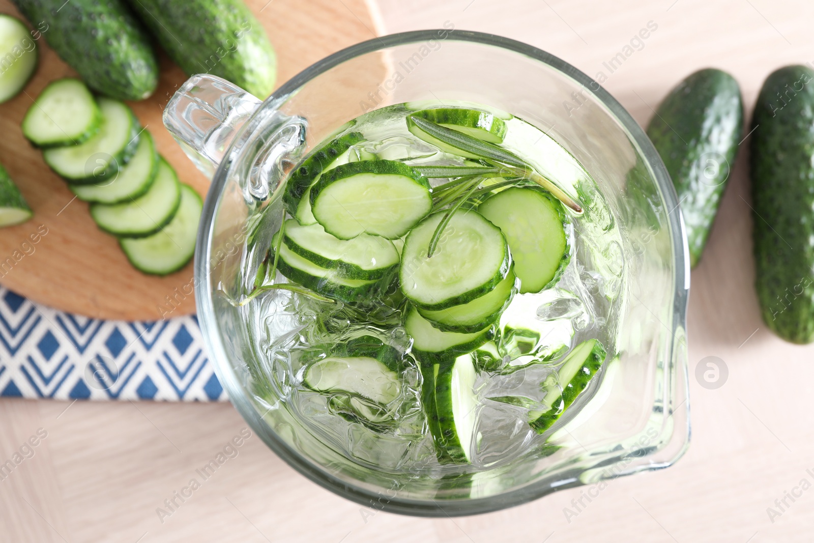 Photo of Refreshing cucumber water with rosemary in jug and vegetables on light wooden table, flat lay