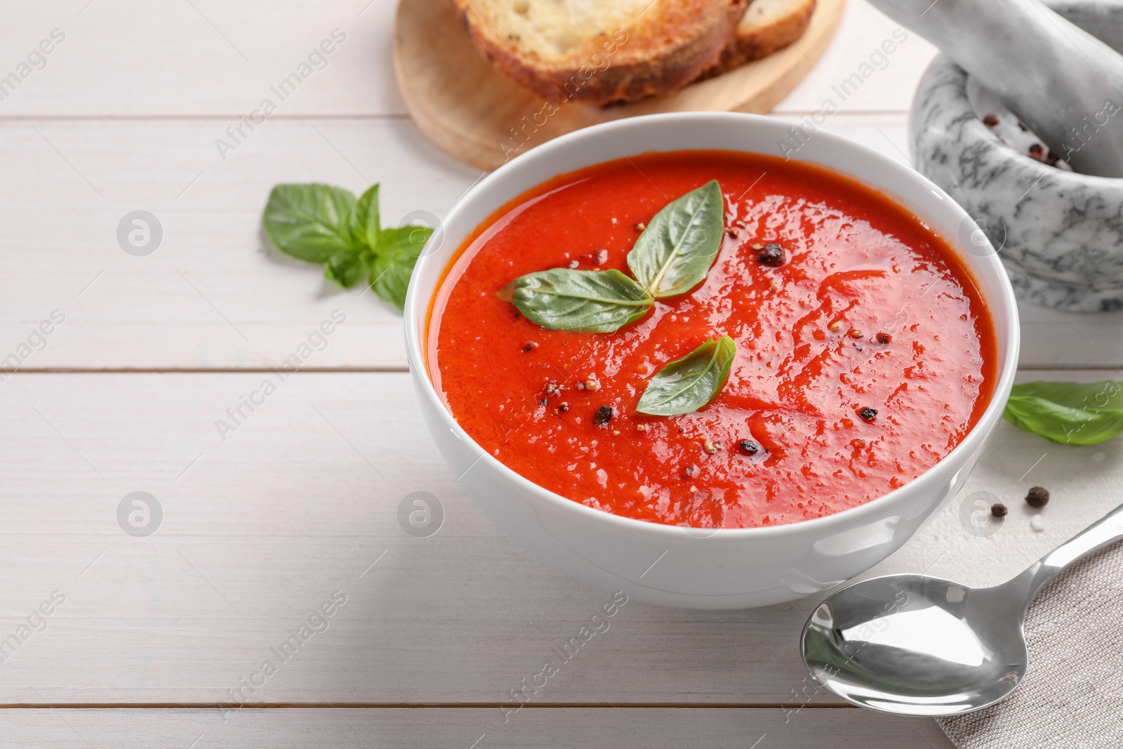 Photo of Delicious tomato cream soup in bowl on white wooden table, space for text