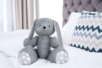 Photo of Cute toy rabbit sitting on bed indoors