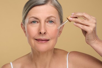 Photo of Senior woman applying cosmetic product on her aging skin against beige background. Rejuvenation treatment