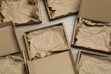 Many open cardboard boxes with crumpled paper on wooden background, flat lay