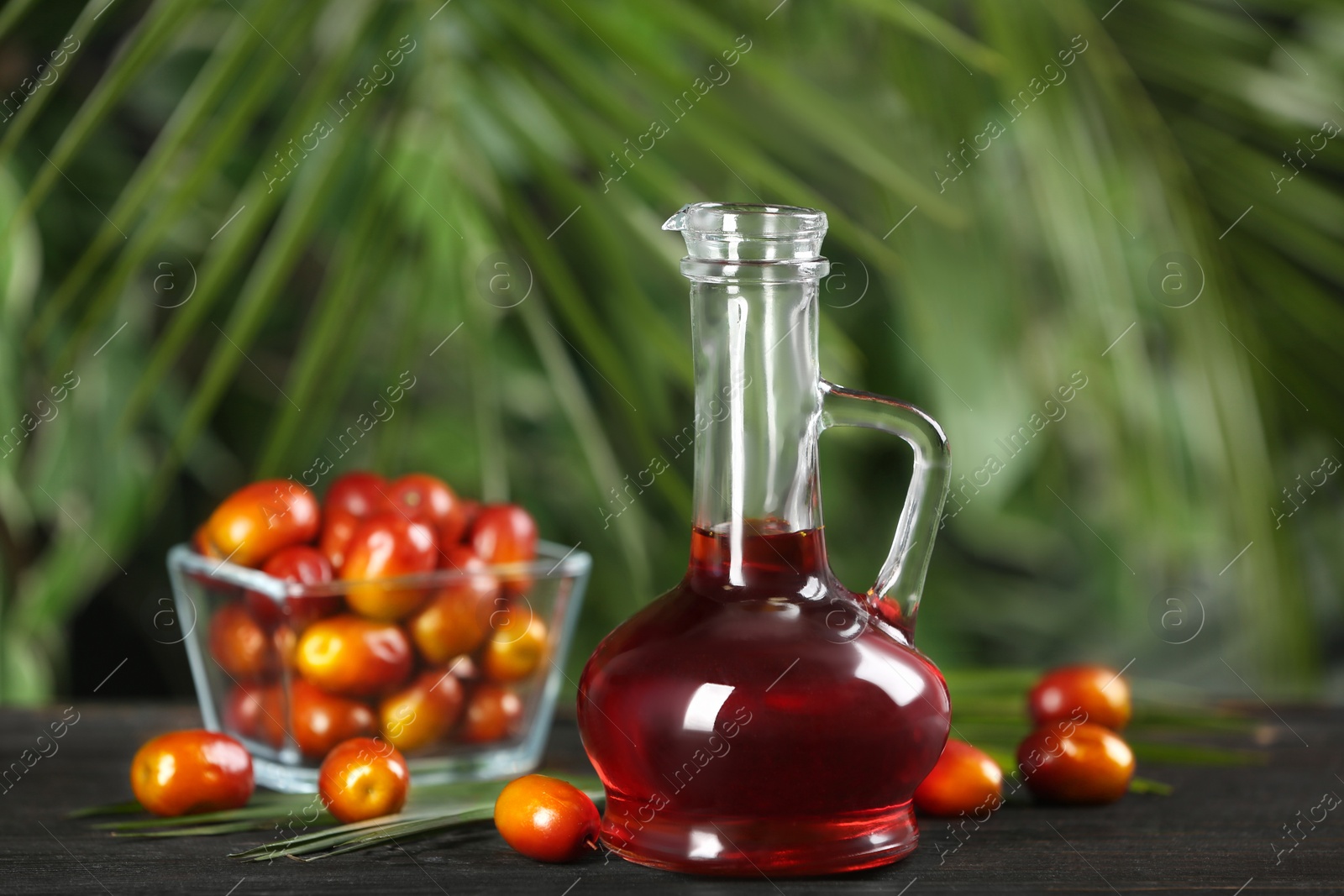 Photo of Palm oil in glass jug, tropical leaf and fruits on wooden table