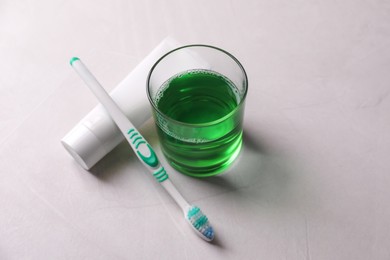 Photo of Fresh mouthwash in glass, toothpaste and toothbrush on light background