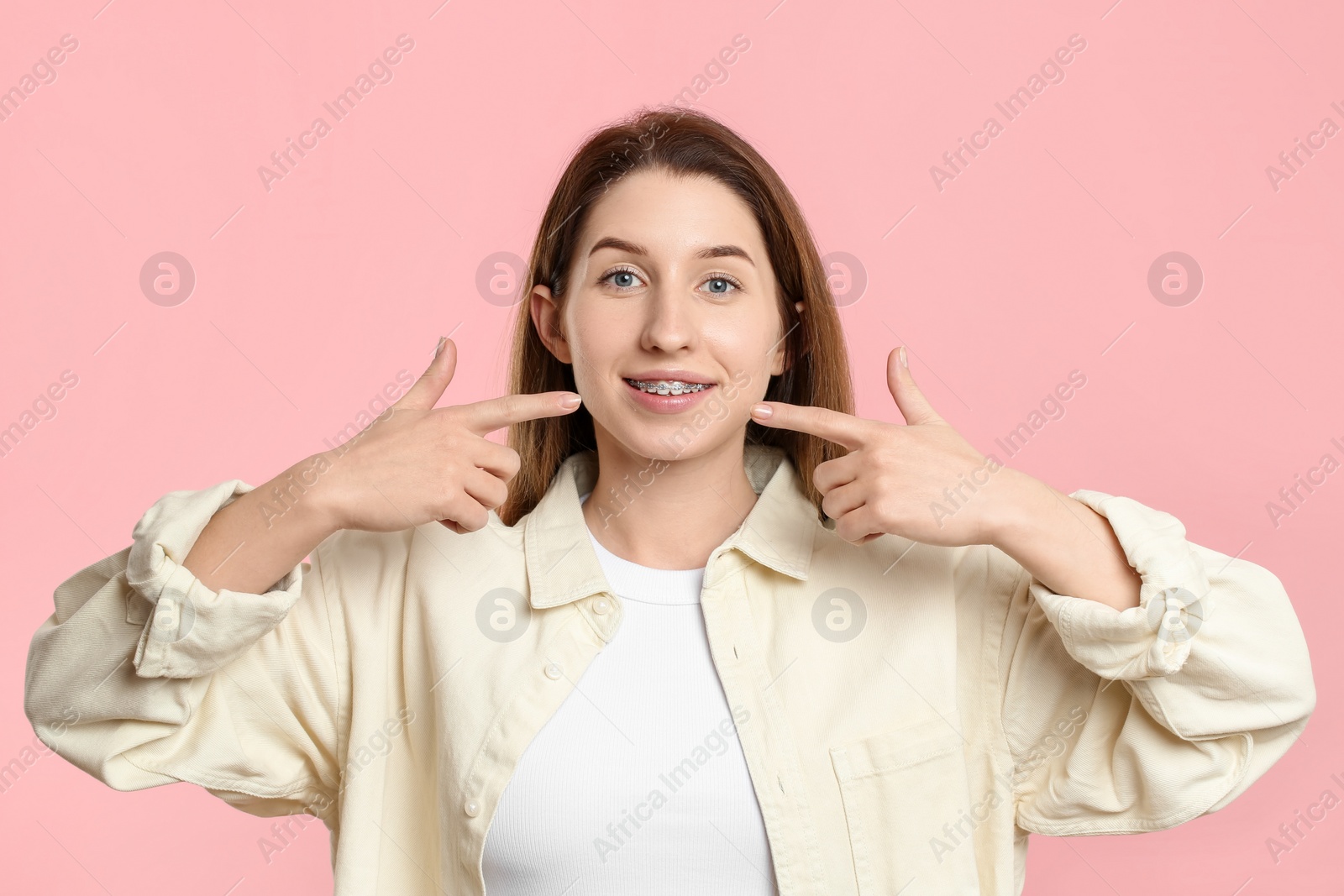 Photo of Portrait of smiling woman pointing at her dental braces on pink background