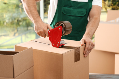 Photo of Man packing box with adhesive tape indoors, closeup. Moving service